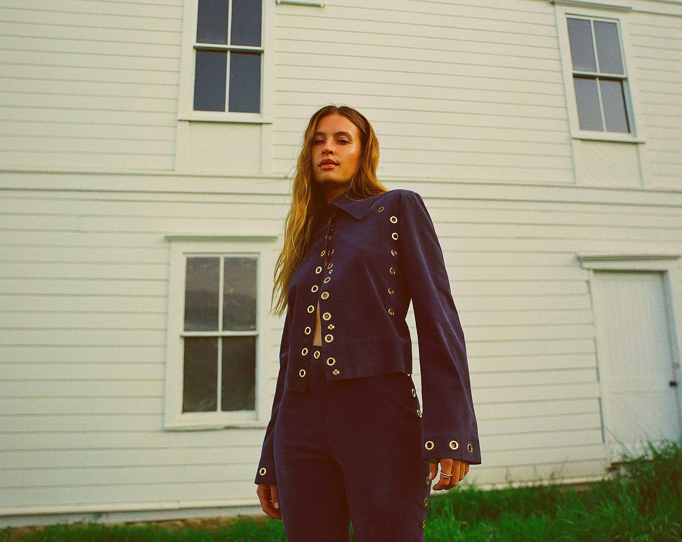 fashion model showcasing a navy outfit with eyelet details against a white wooden building
