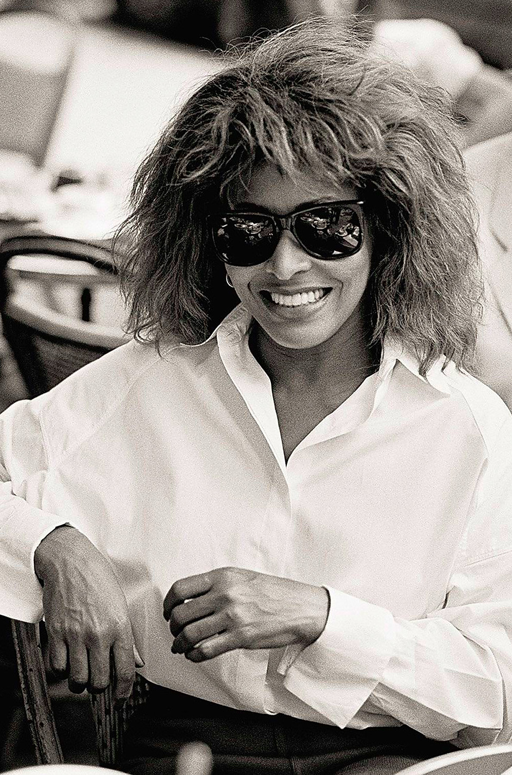 tina turner wearing a white shirt and sunglasses, seated at a table