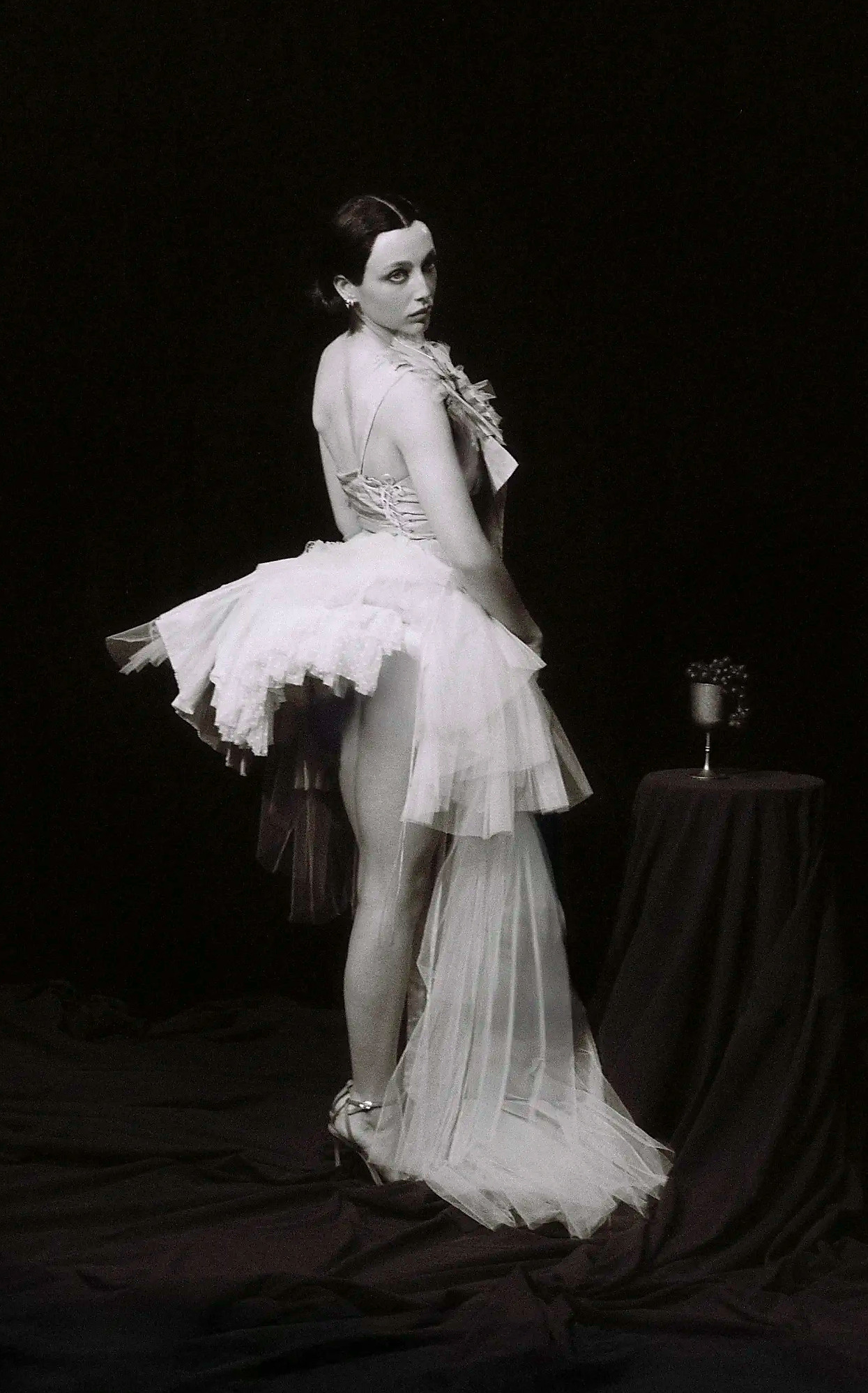 Emma Chamberlain posing from behind in a victorian dress with black hair and a ribbon that says Miss Claire Sullivan