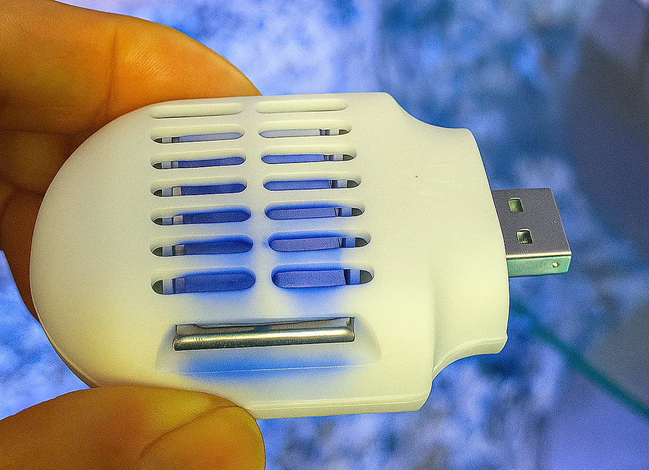 A hand holding a small, white, USB-powered mosquito repeller.