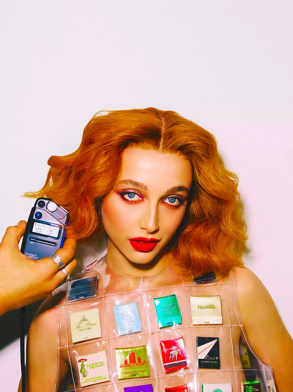 Emma Chamberlain posing with a light meter, matchbox dress in a red wig