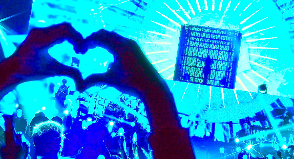 Fan making a heart with their hands as Ado performs on stage