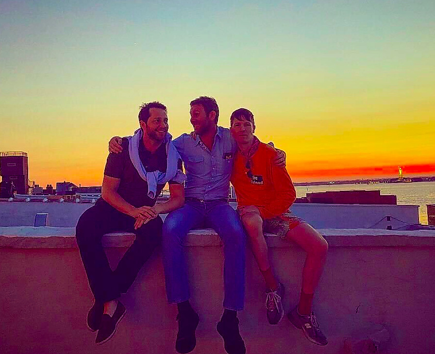 friends sitting on a rooftop at sunset with a view of the skyline and water
