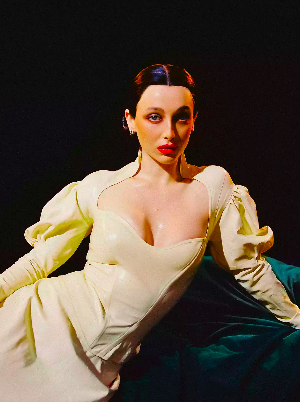 Emma Chamberlain in a latex dress lounging on green velvet