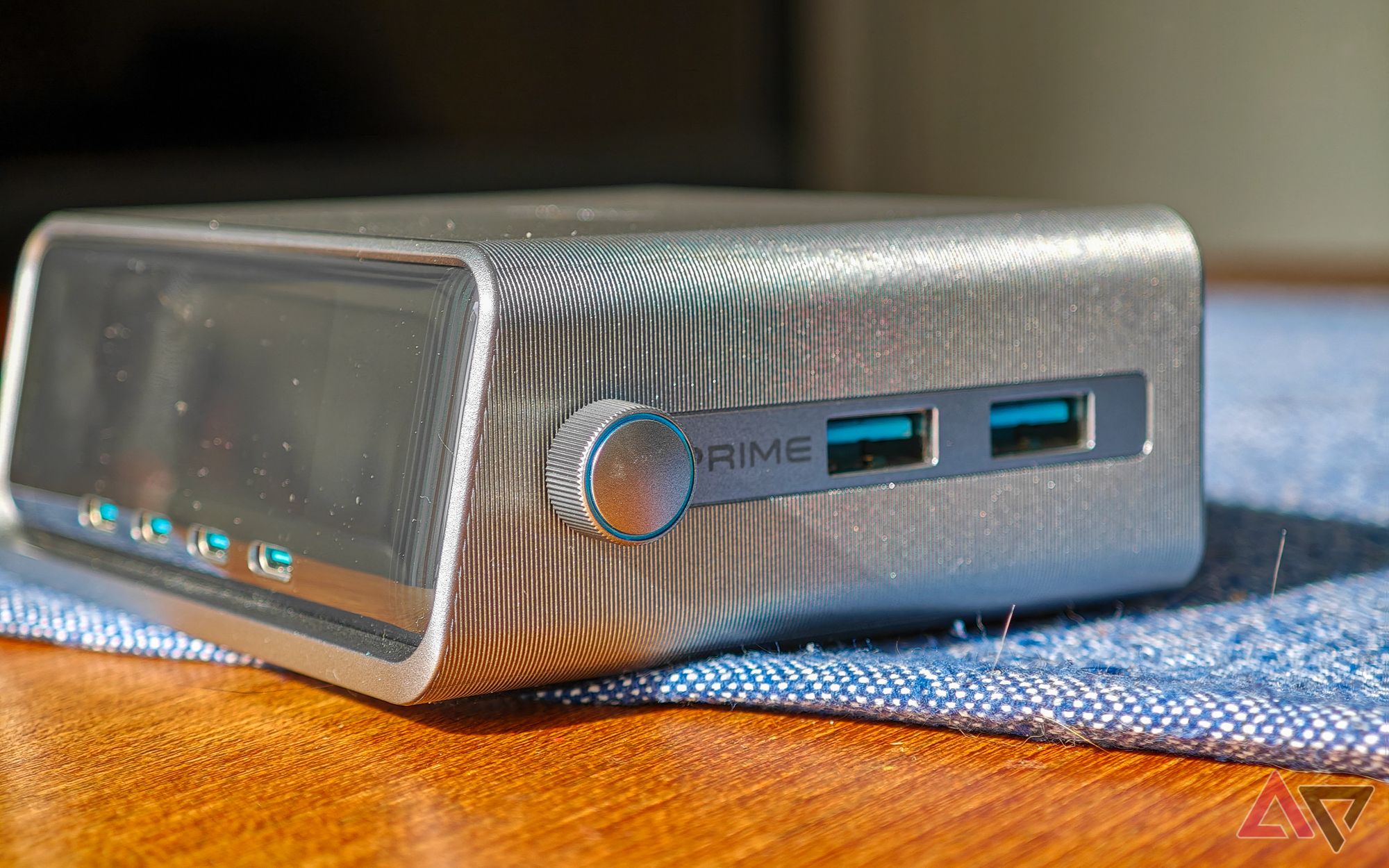 Anker Prime 250W desktop charger sitting on a blue cloth on a wooden table, seen at an angle to show all six USB ports and control knob