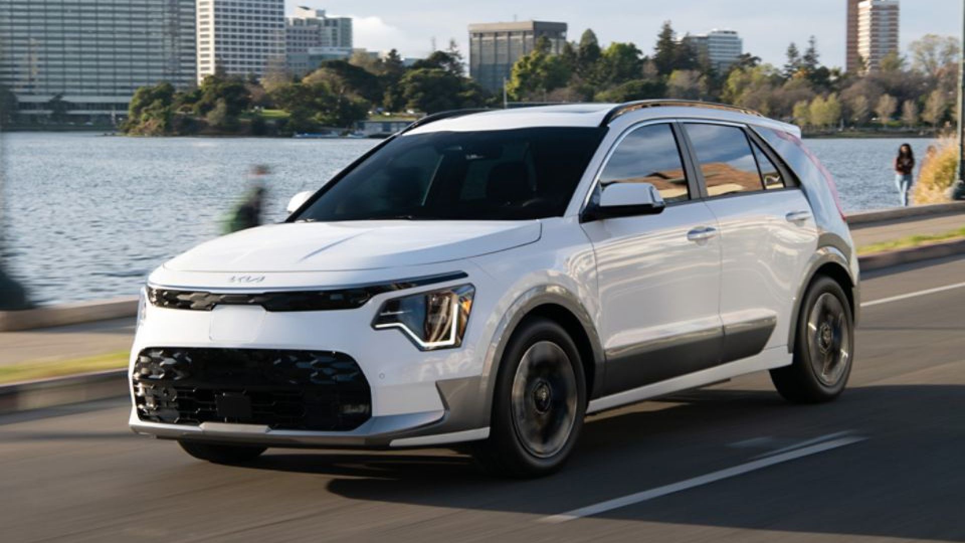 White 2024 Kia Niro EV driving down the road in front of water