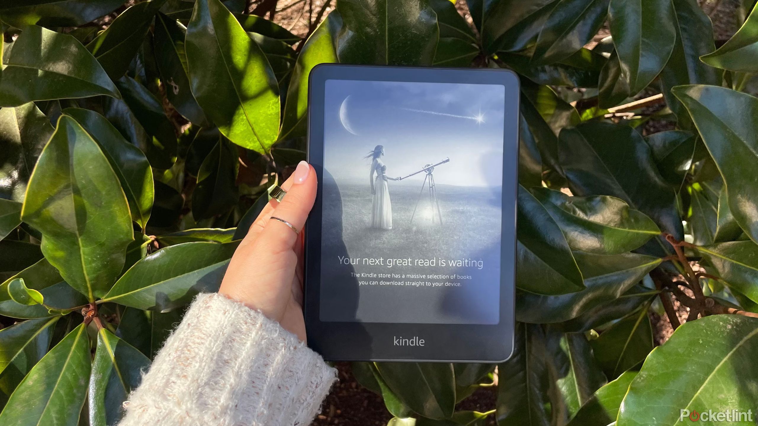 A woman holding a kindle paperwhite 2024 in front of foliage. 