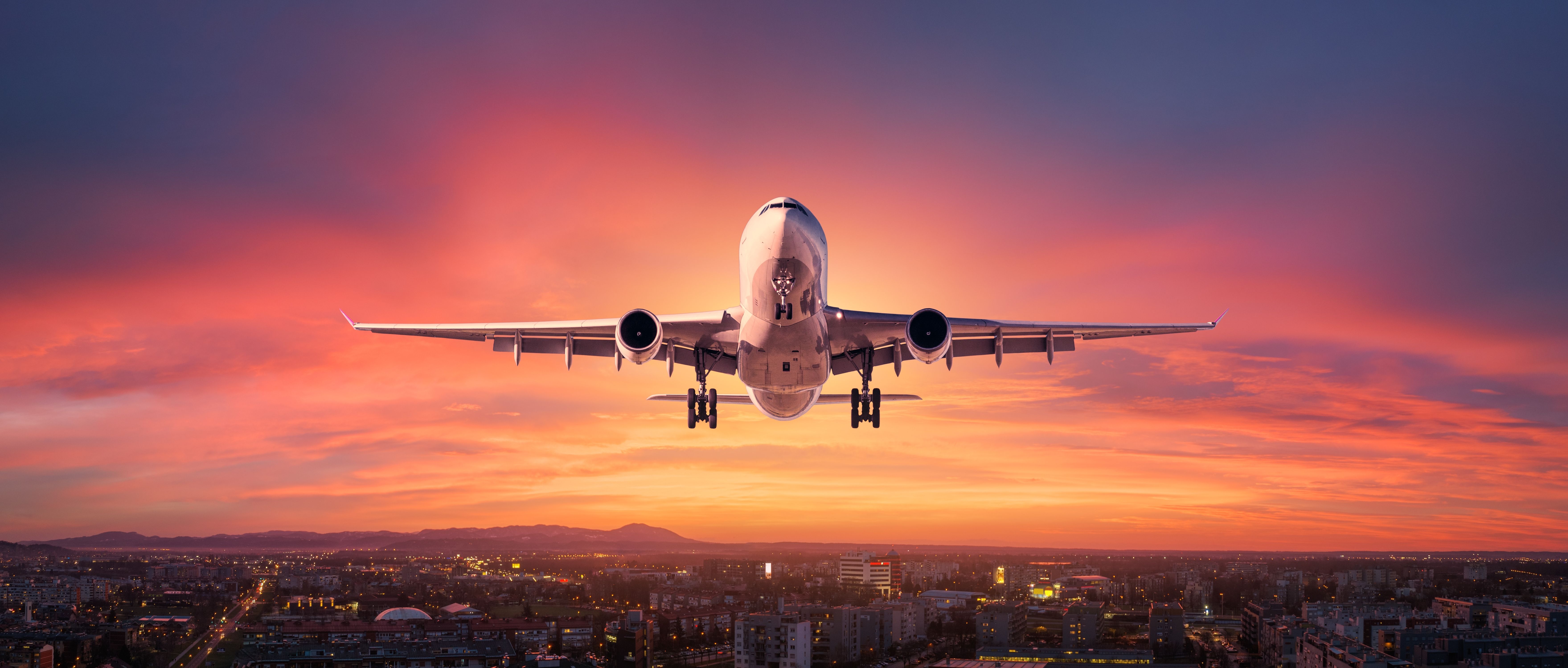 Airplane flying over a city at sunset