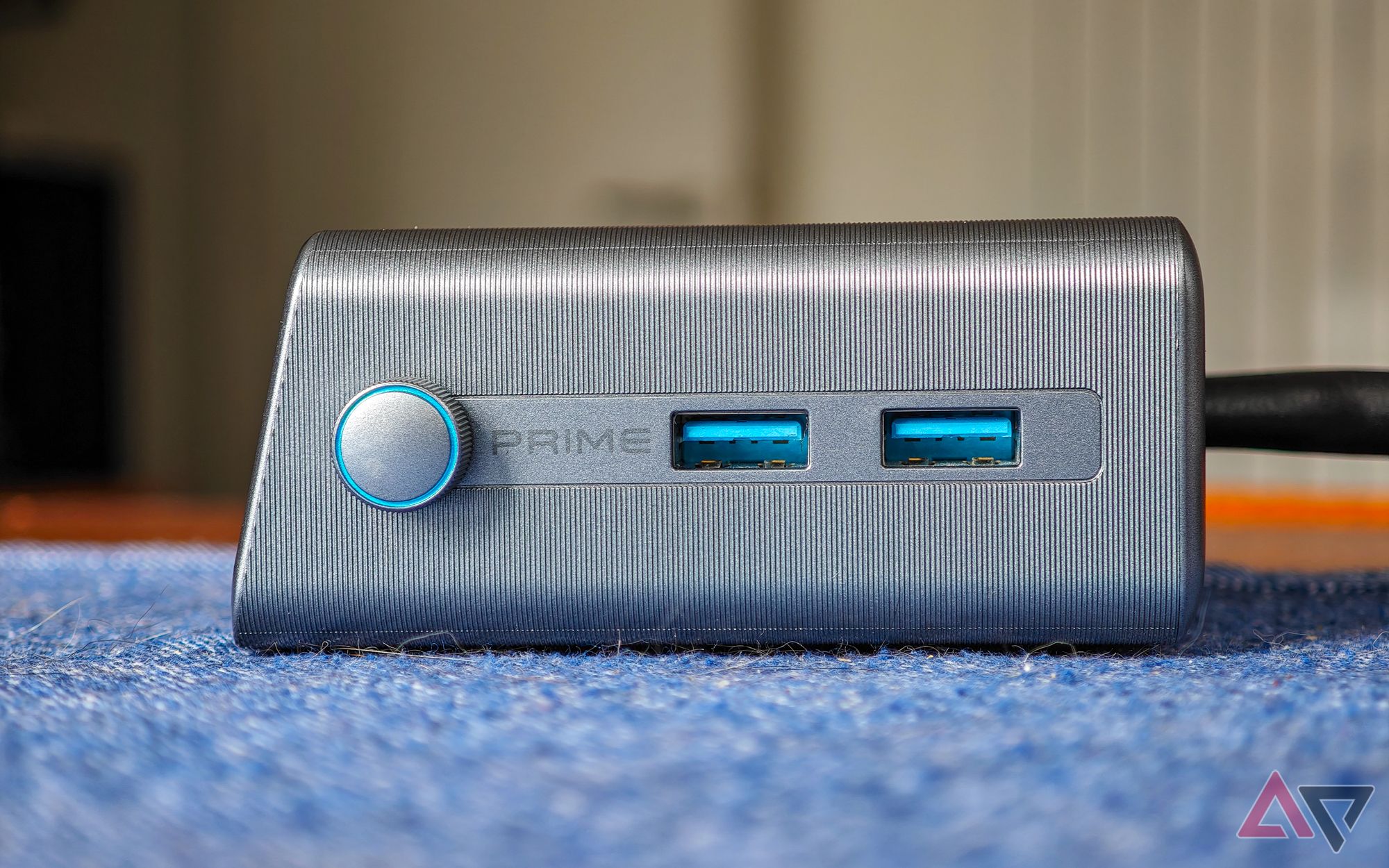 Anker Prime 250W desktop charger sitting on a blue cloth on a wooden table seen from the side showing two USB-A ports and a control knob